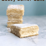A slice of gooey butter cake, in front of a stack of slices. Text overlay reads "St. Louis Gooey Butter Cake. Yeasted Dough. Bakery-Style. Easy As Cookies."