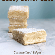 A slice of gooey butter cake, in front of a stack of slices. Text overlay reads "St. Louis Gooey Butter Cake. Caramelized Edges. Gooey Center. Easy As Cookies."