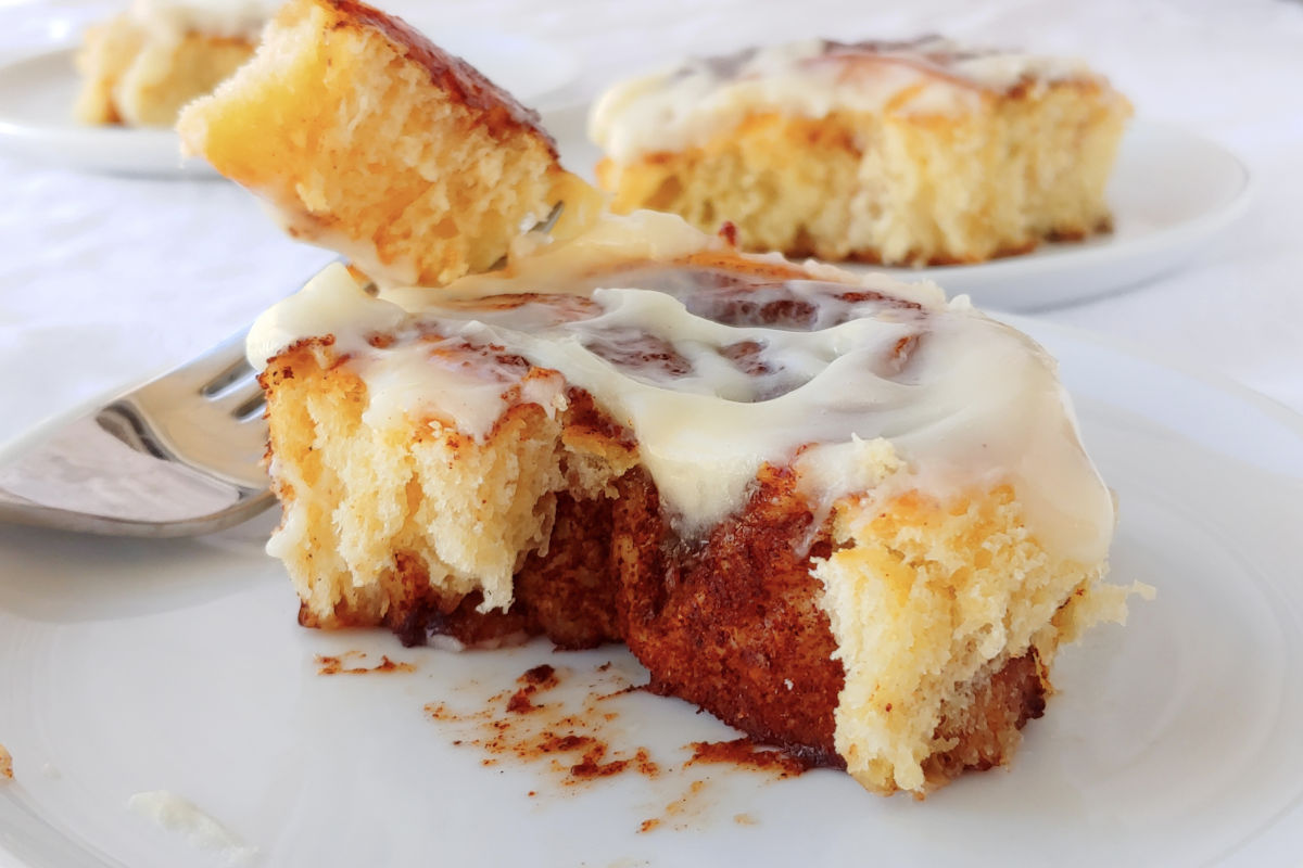 Overnight cinnamon roll torn apart to show the swirl of brown sugar cinnamon. A fork holds a bite next to it.