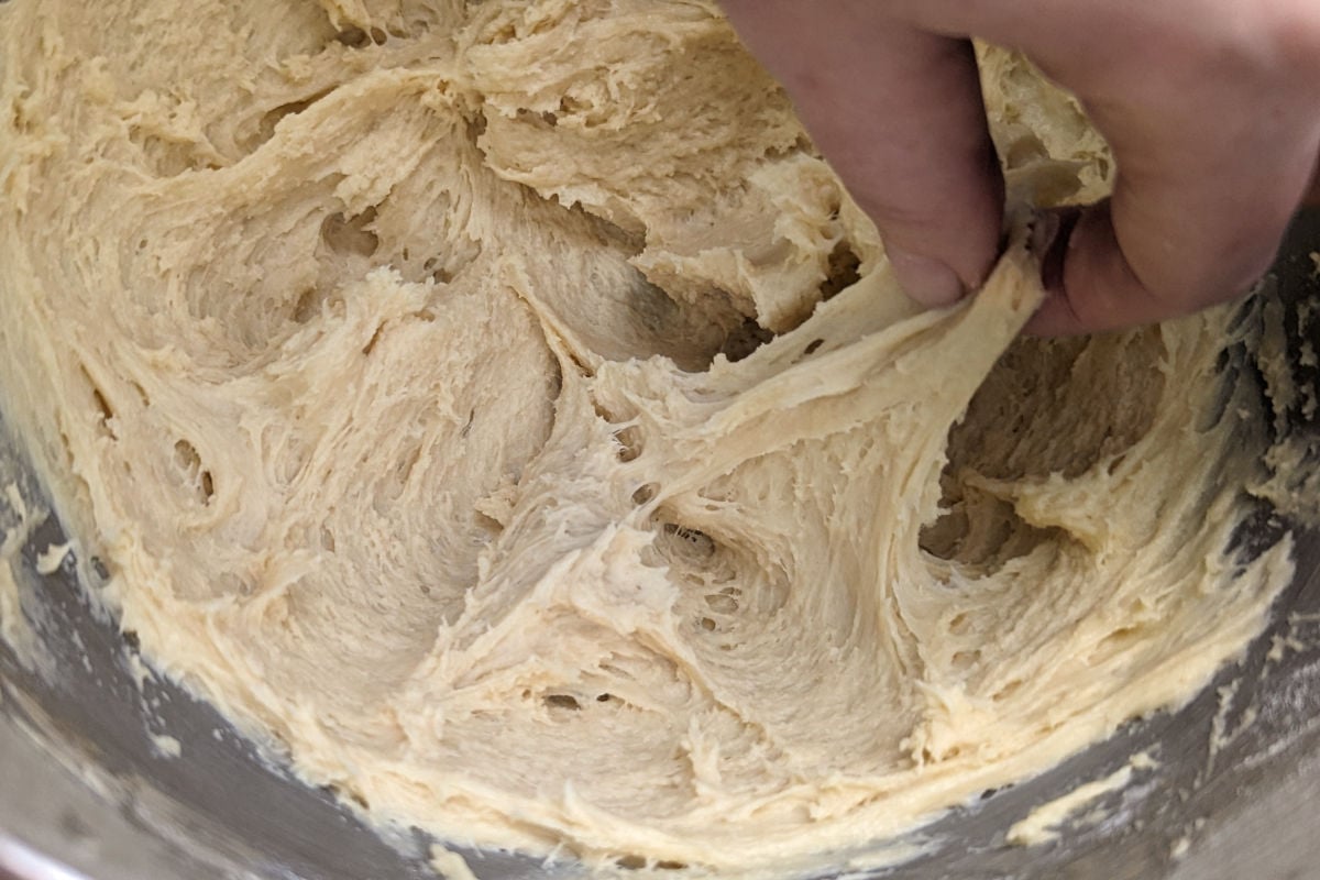 A hand stretches yeasted dough for St. Louis Gooey Butter Cake.