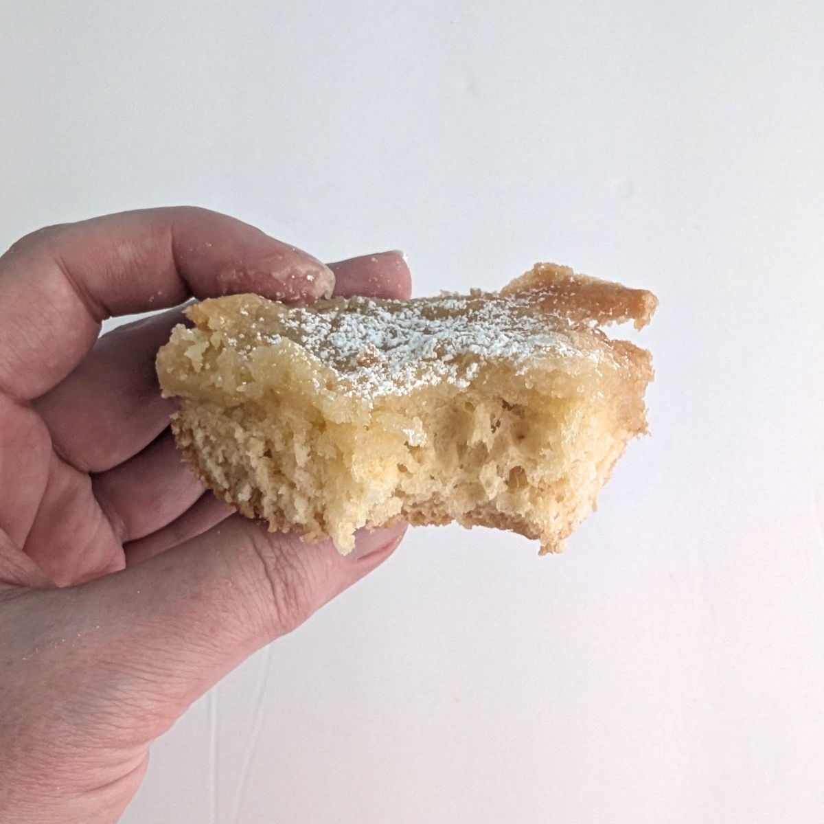 A hand holds a slice of gooey butter cake, which is missing a bite.