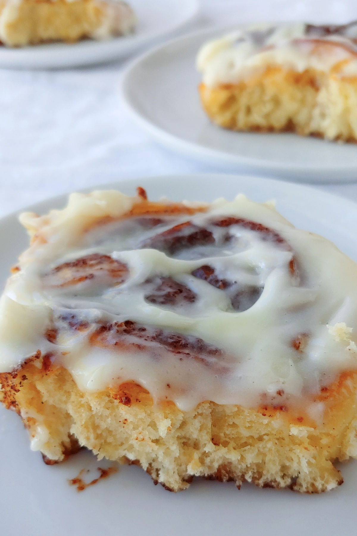 An overnight cinnamon roll with cream cheese glaze on top. Other cinnamon rolls in the background.
