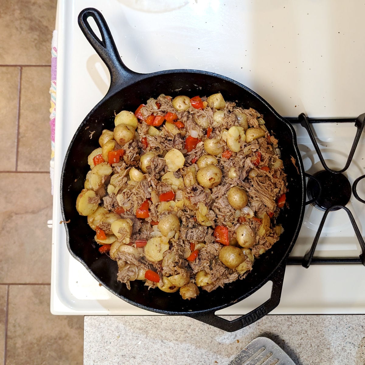 Cooked roast beef hash in a cast iron skillet on a stove.