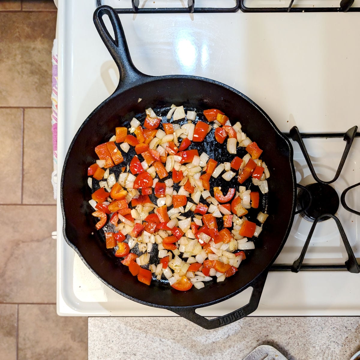Chopped peppers and onions in a cast iron skillet, turning translucent after cooking.
