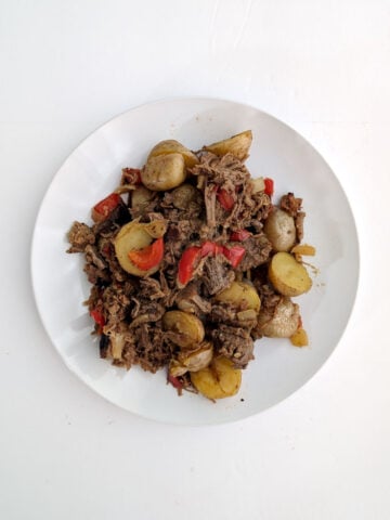 Roast beef hash with peppers and onions on a white plate.