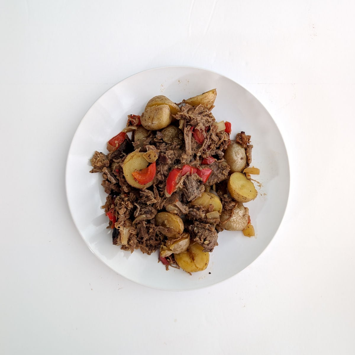 Roast beef hash with peppers and onions on a white plate.