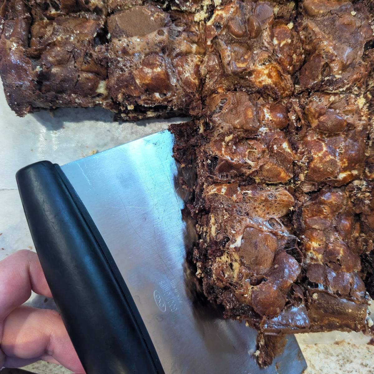 A bench scraper lifts cut s'mores brownies from parchment paper.