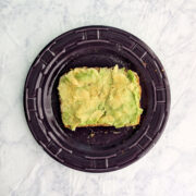 A slice of avocado toast on a purple plate.