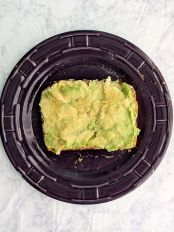 A slice of avocado toast on a purple plate.