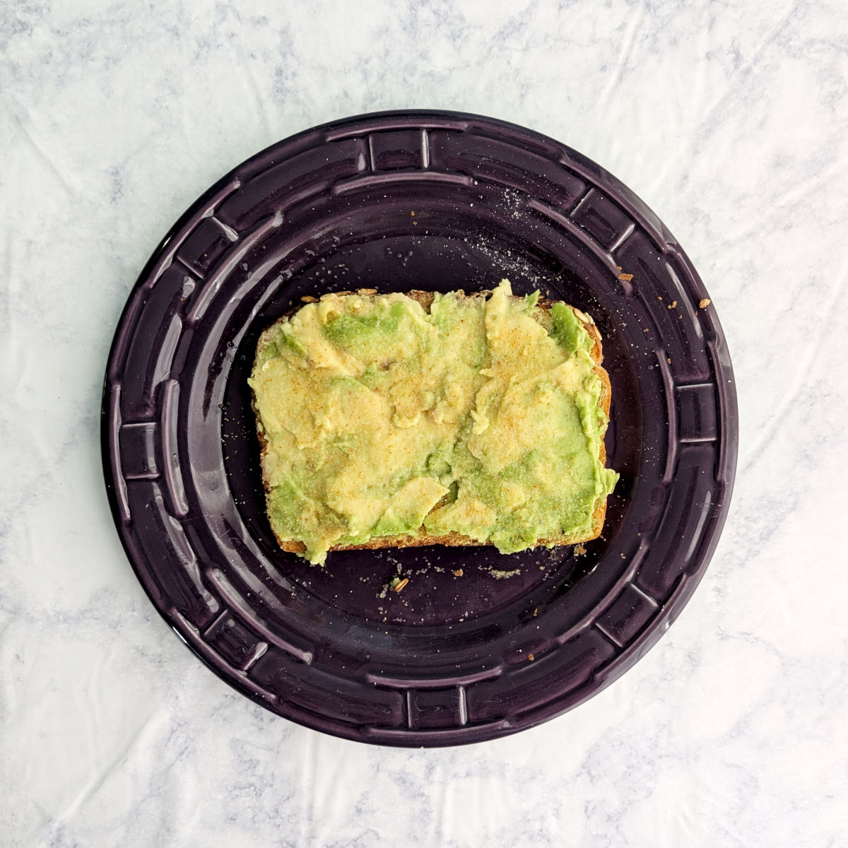 A slice of avocado toast on a purple plate.