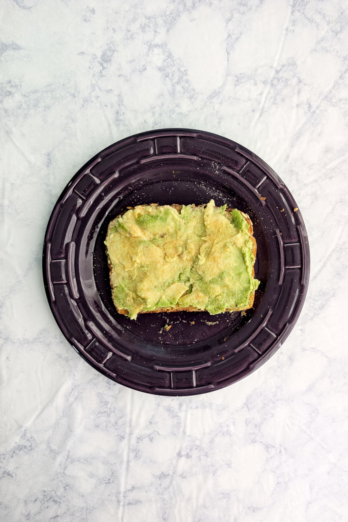 A slice of avocado toast on a purple plate.