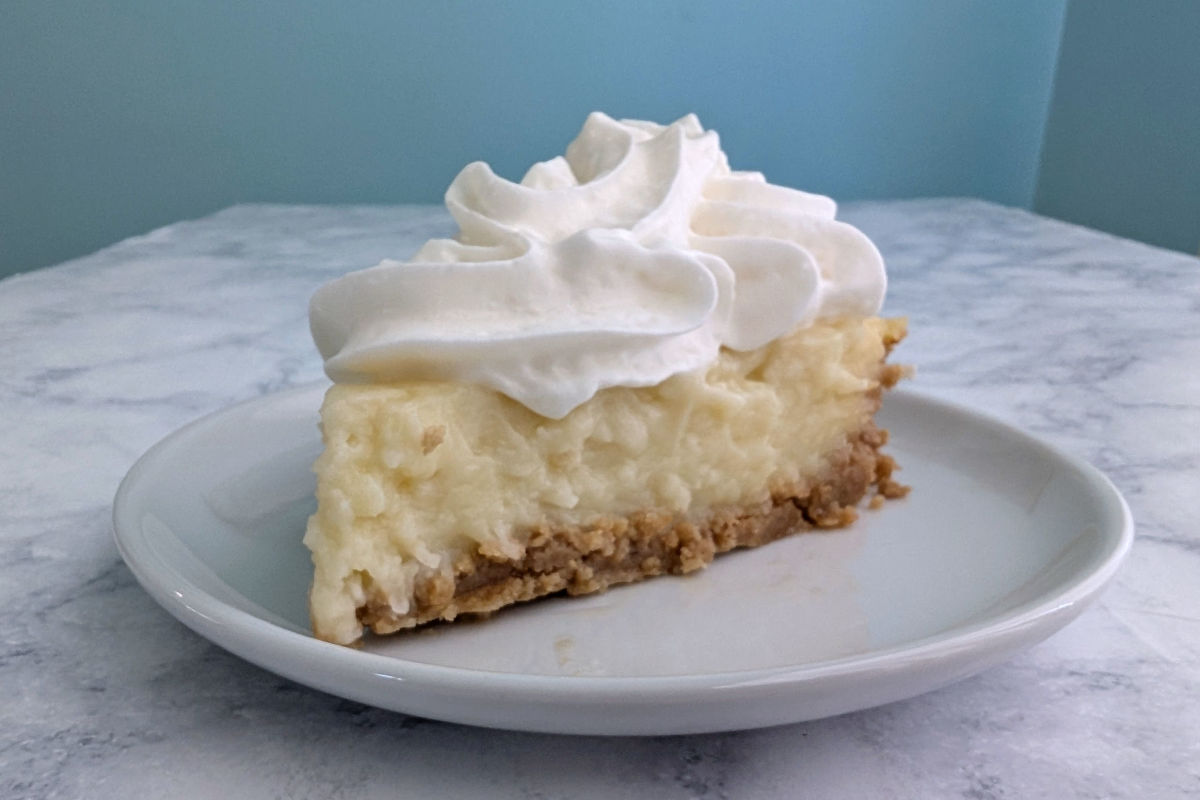 Slice of coconut cream pie topped with whipped cream, on a plate.