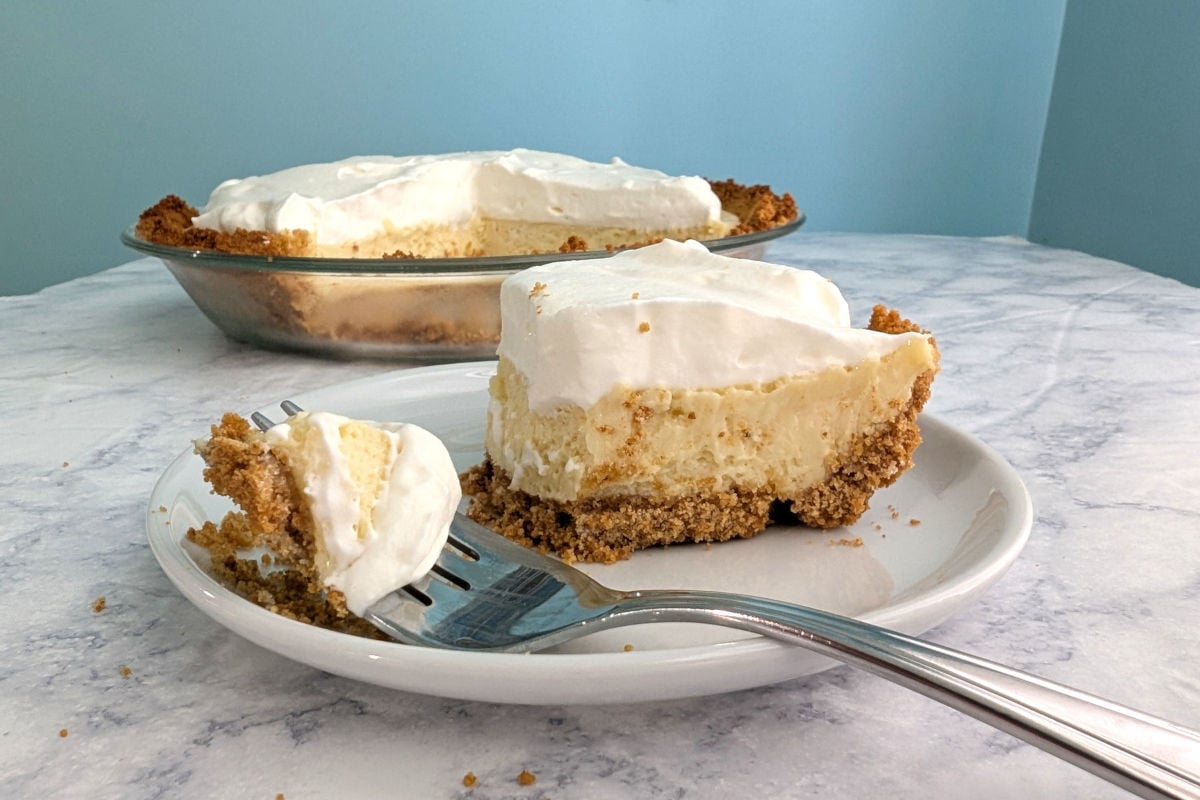 A fork with a bite of key lime pie rests on a plate with the rest of the slice of pie.