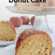 A slice of apple cider donut cake is on a plate, in front of another slice on a plate. The full cake is in the background. Text overlay reads "Apple Cider Donut Cake. Easy As Cookies."