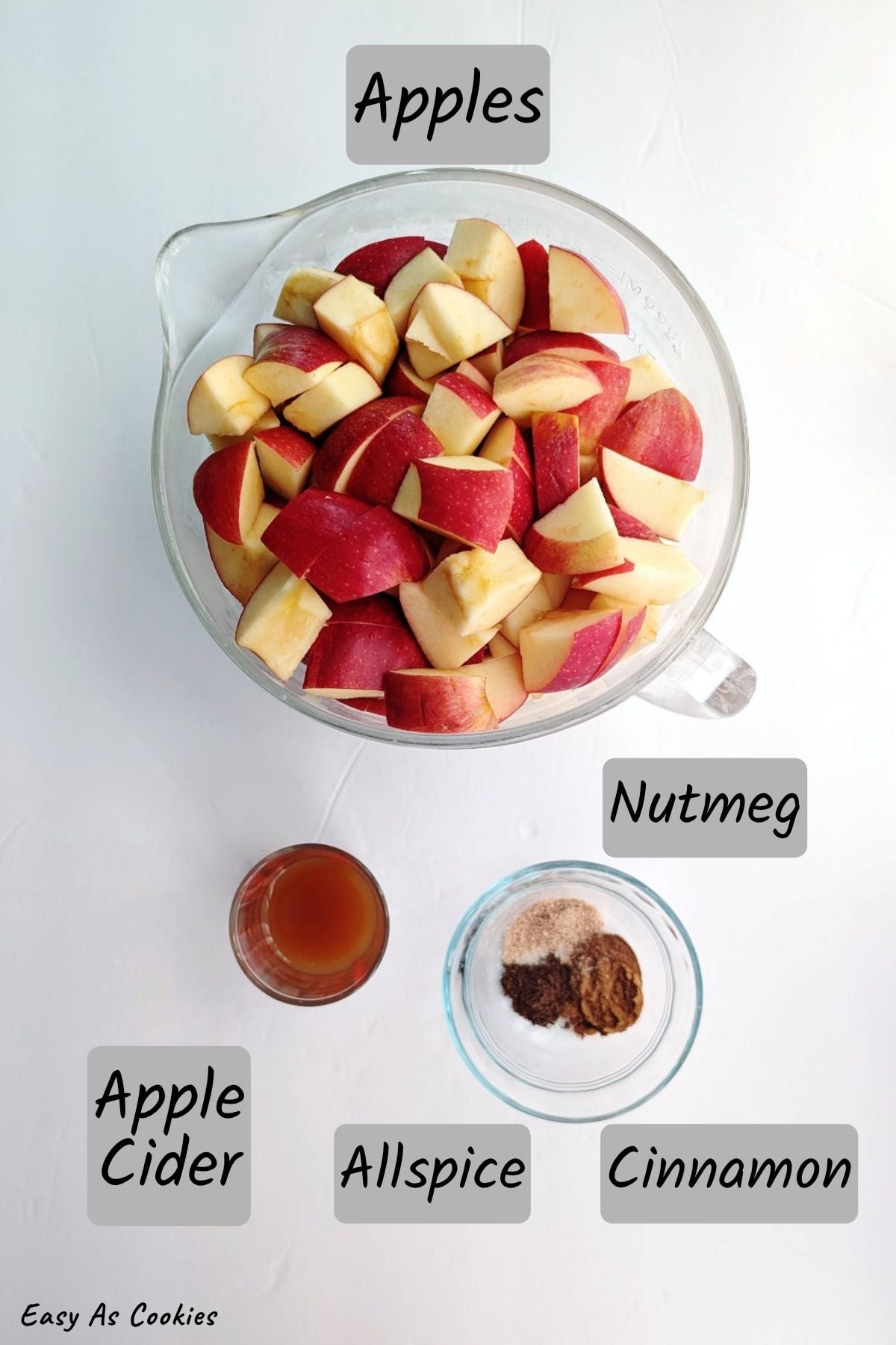 Labeled photo of ingredients for slow cooker apple butter with no added sugar: chopped apples, apple cider, allspice, cinnamon, and nutmeg.