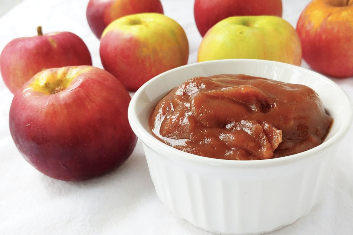 Slow cooker apple butter in a white ramekin, next to several apples.