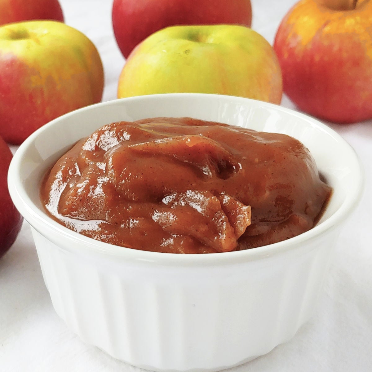 Slow cooker apple butter in a white ramekin, next to several apples.
