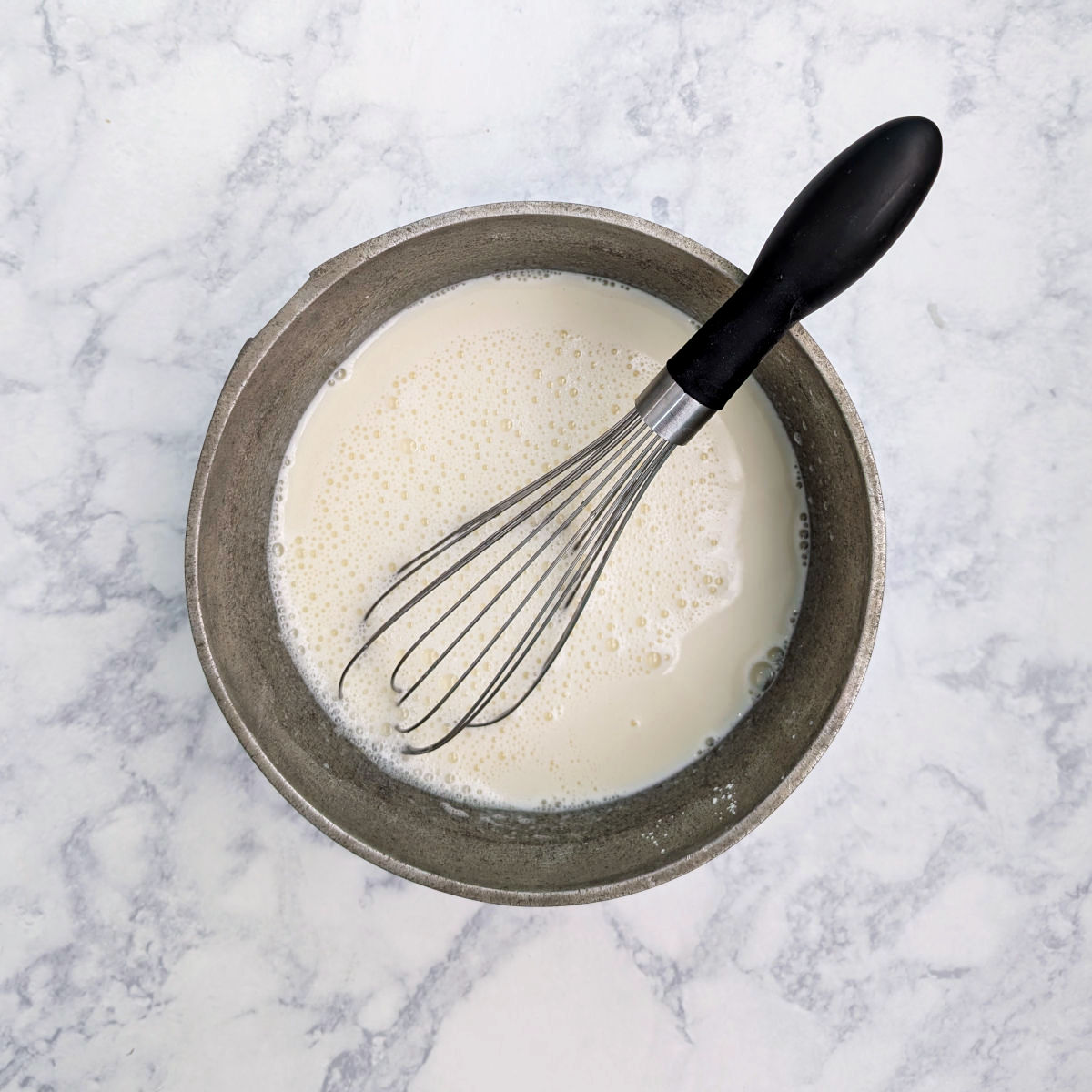 Egg mixture with milk whisked into it, in a saucepan with wire whisk.