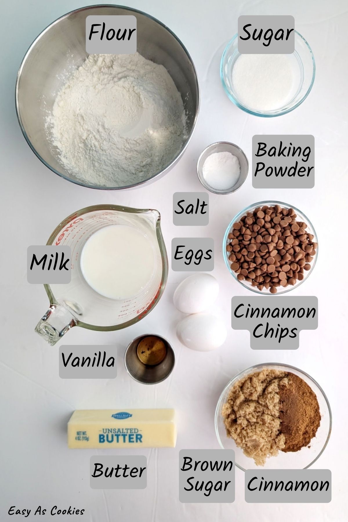 Labeled photo of ingredients for Layered Cinnamon Scones, including flour, sugar, baking powder, salt, milk, vanilla, cinnamon chips, butter, eggs, brown sugar, and cinnamon.