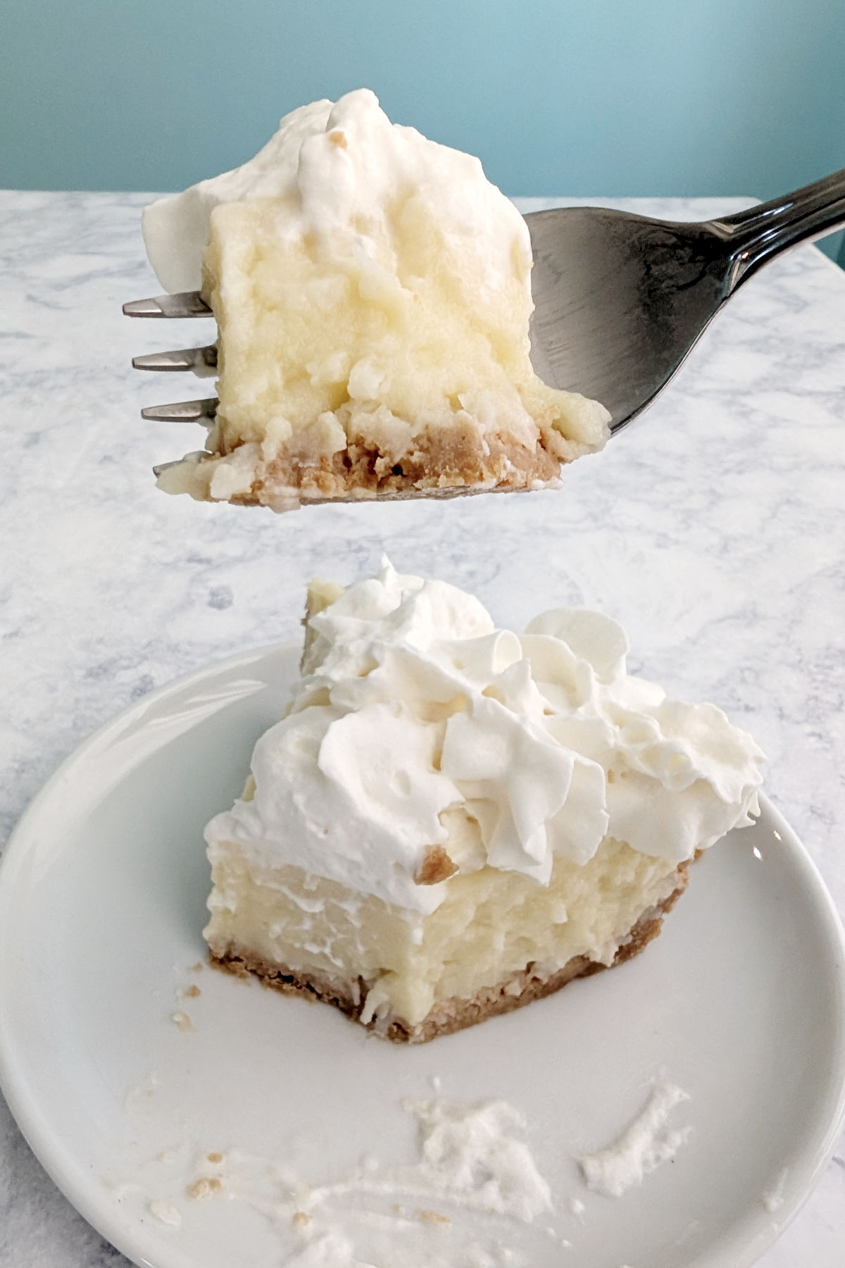 A bite of coconut cream pie on a fork, held over the slice of pie.