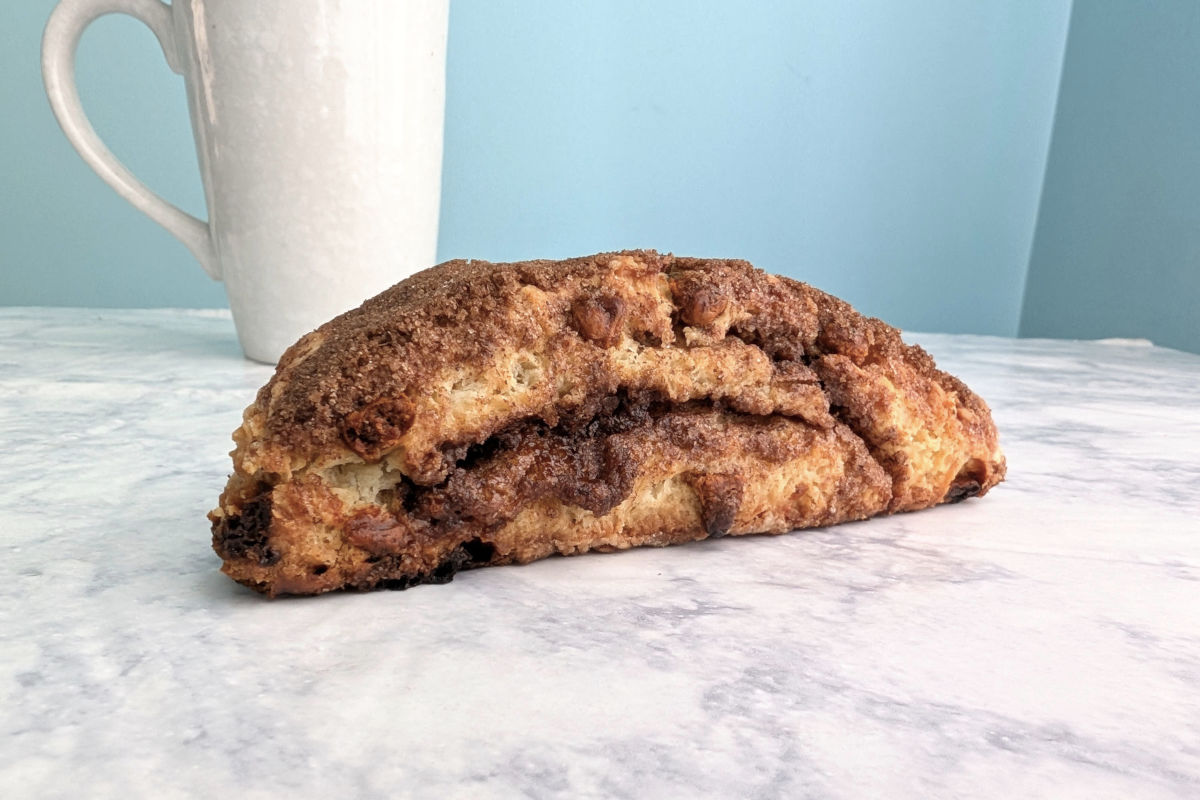A layered cinnamon scone, seen from the side to see layers. A mug is in the background.