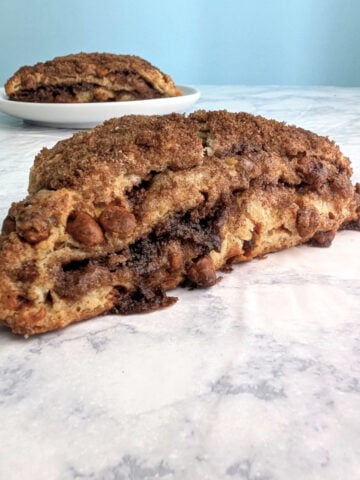 A layered cinnamon scone, seen from the side to see layers. Another scone on a plate is behind it.