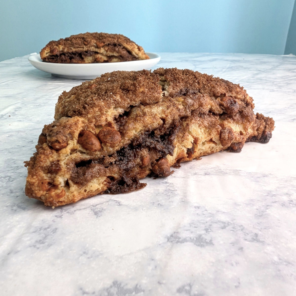 A layered cinnamon scone, seen from the side to see layers. Another scone on a plate is behind it.