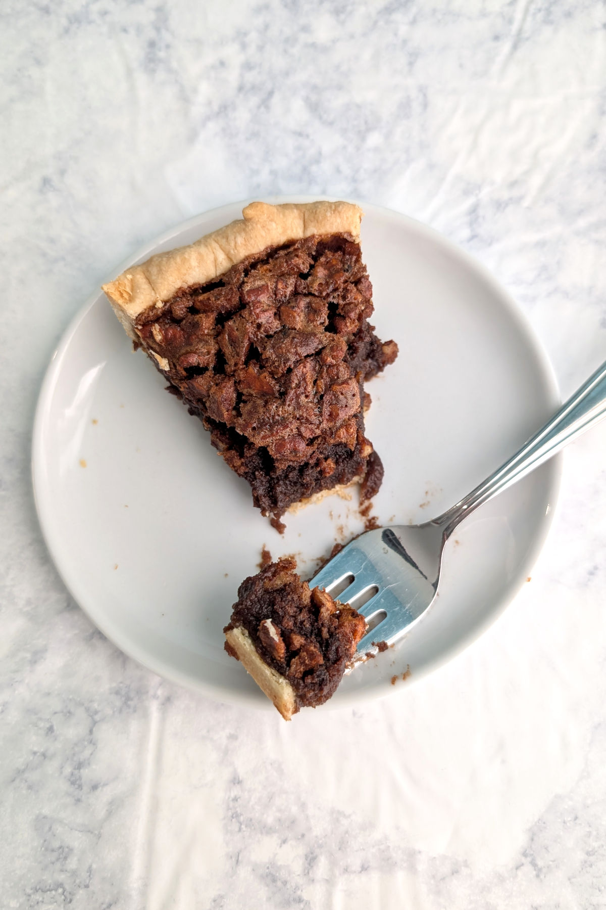 A bite of pecan fudge pie on a fork to show texture. Fork rests on the plate with the remaining slice of pie.