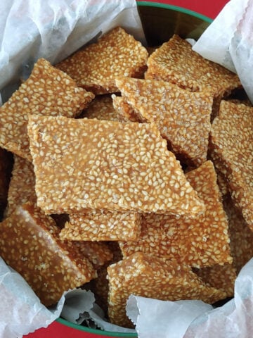 Pieces of homemade sesame brittle in a tin lined with waxed paper.